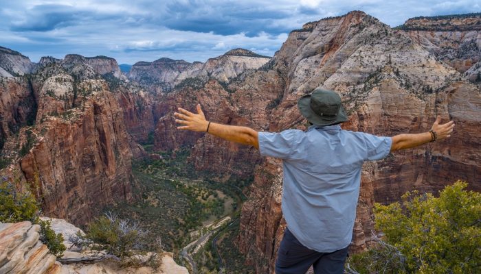 A male standing on top of the rock formations with stretched arms in Zion National Park, USA